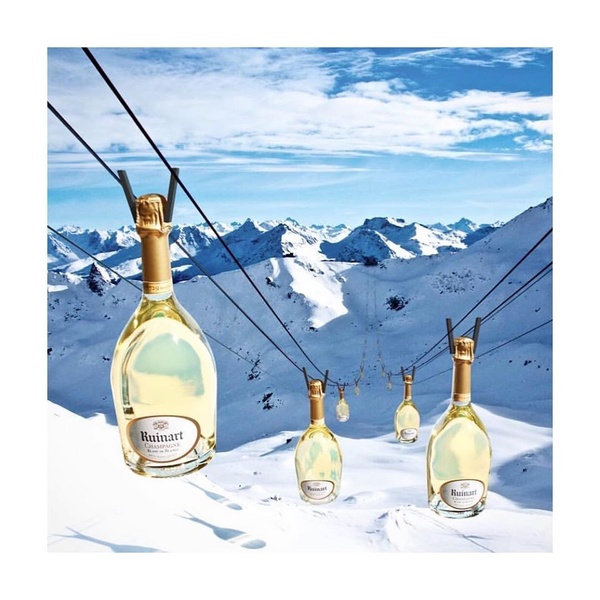 A visually striking composition featuring multiple Champagne bottles suspended like cable cars against a bright, snowy mountain landscape.