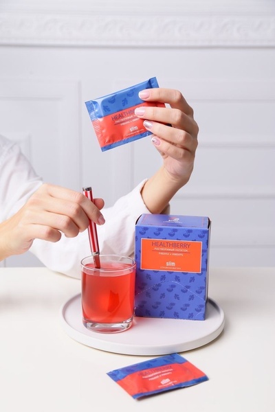 A close-up view of a hand preparing a red berry drink from a packet, showing the sachet, the drink, and the packaging box.