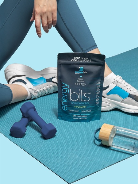 A clean, studio-lit hero shot of spirulina tablets placed on a yoga mat with workout accessories to emphasize fitness.