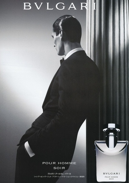 A sophisticated, high-contrast monochrome advertisement featuring a well-dressed man leaning against a pillar, highlighting the Bvlgari Pour Homme Soir bottle.