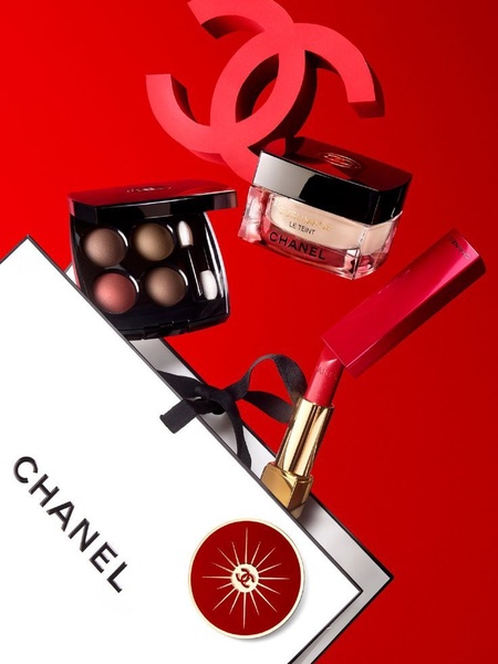 A high-end studio shot of a cosmetic collection featuring an eye palette, foundation jar, and lipstick, elegantly positioned near a branded shopping bag.
