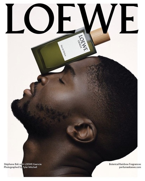A high-fashion, minimalist portrait featuring a bottle of fragrance balanced on a man's forehead.