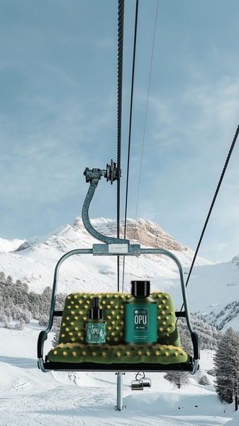 A high-end skincare serum set is placed on a green, cactus-like textured ski lift seat against a stark, snow-covered mountain backdrop.