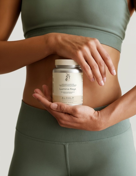 A close-up photograph featuring a woman in sage green activewear holding a bottle of Lumina Rays dietary supplement against her stomach.