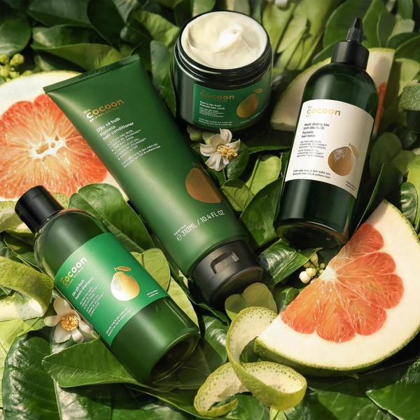 A high-angle, flat-lay photography shot of pomelo-infused hair care products nestled among fresh green leaves and sliced fruit.
