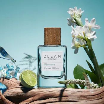 A 1:1 square format creative featuring a perfume bottle centered against a soft blue background, surrounded by natural elements like white flowers, a lime slice, and driftwood.