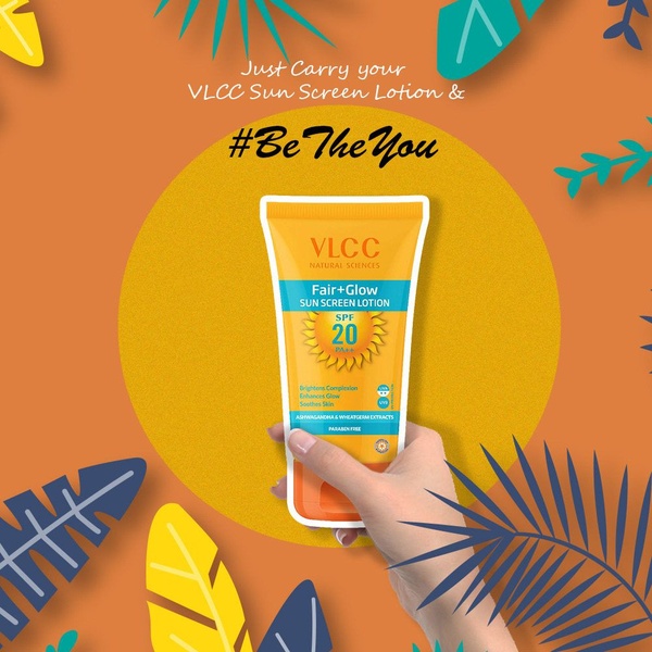 A close-up hand holding a sun screen lotion tube against an orange background with paper-cut style tropical leaves, promoting a radiant skin glow.