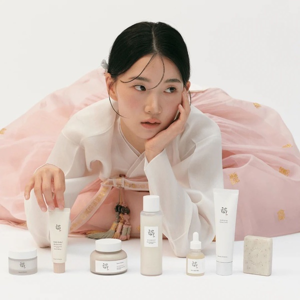 A clean, studio-lit photograph showcasing a complete collection of skincare products arranged neatly in front of a model wearing a traditional hanbok.