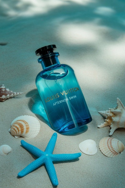 A luxury perfume bottle sits centered on soft white sand, surrounded by natural seashells and a starfish, evoking a clean, summer-ready aesthetic.