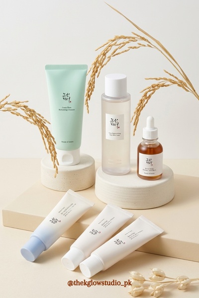 A clean, high-end product photography shot featuring a skincare line organized on pedestals, accented with dried wheat elements.