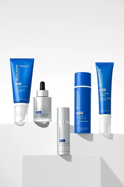 A high-end, minimalist studio photograph featuring a curated collection of skincare products arranged on tiered white platforms.