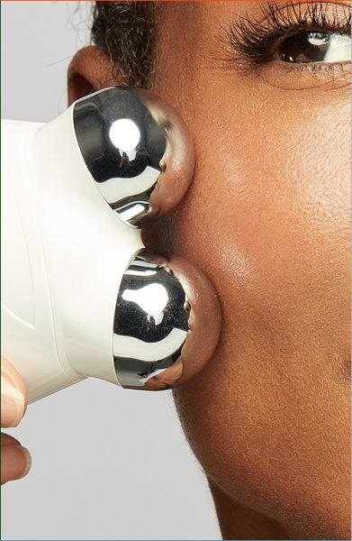 An intimate, macro-view shot showing a facial sculpting device being applied to a model's cheek, emphasizing skin texture and product contact.
