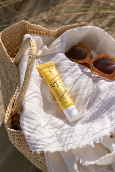 A high-angle aesthetic shot of a sunscreen tube tucked inside a woven beach bag with sunglasses, capturing a premium summer lifestyle vibe.