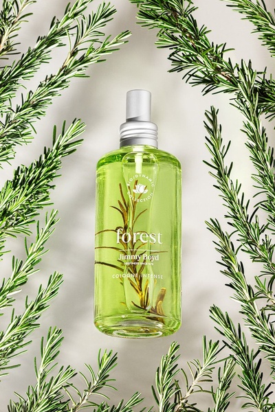 A high-quality, top-down shot of a glass cologne bottle surrounded by fresh green rosemary sprigs, emphasizing a natural and organic brand identity.