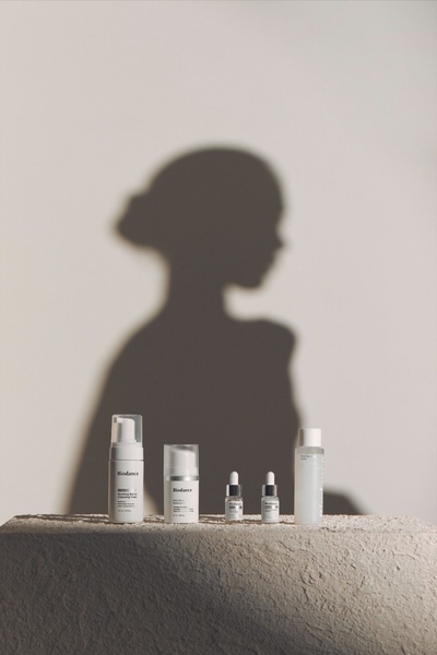 A high-end, clean studio shot of a four-piece skincare set featuring an elegant human silhouette shadow backdrop to evoke a premium, aspirational mood.