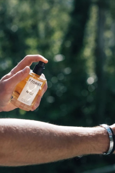 A close-up, high-quality shot of a hand spraying a bottle of perfume in natural sunlight, emphasizing texture and the sensory experience of the product.
