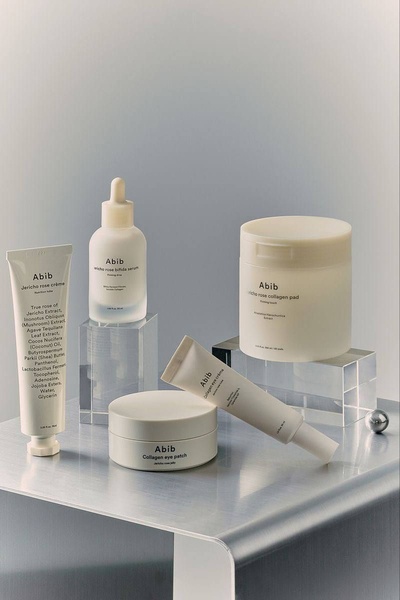 A high-end, studio-lit product photography creative showcasing a full collection of skincare items staged on clear acrylic risers against a clean, neutral backdrop.