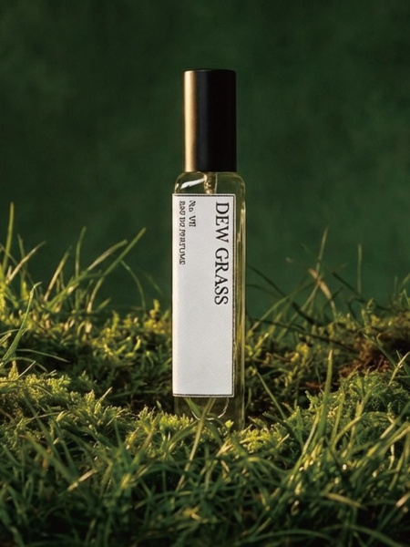 A close-up vertical shot of a perfume bottle labeled Dew Grass, placed directly on a bed of lush green moss to convey a natural and fresh scent profile.