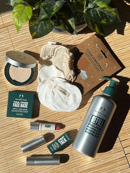A high-angle natural light flatlay showcasing a set of reusable makeup remover pads, face powder, and refillable beauty containers on a bamboo surface.
