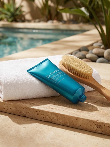 A high-end product hero shot featuring a tube of body moisturizer resting on a white towel against a stone surface by a swimming pool.