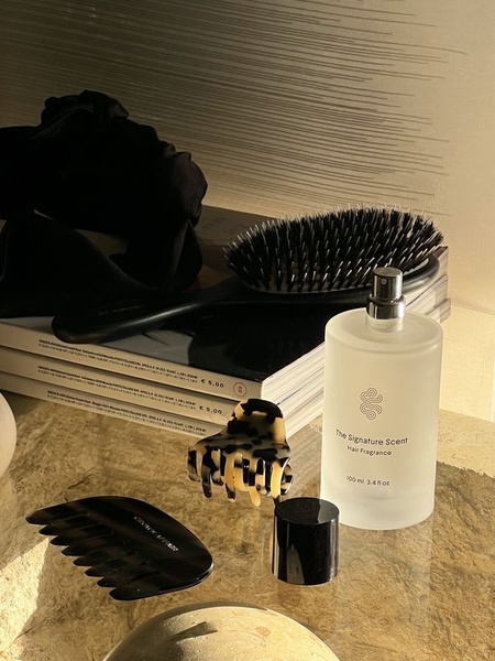 A luxury-focused product shot of a hair fragrance bottle surrounded by professional hair tools on a stone surface, emphasizing an aspirational lifestyle.