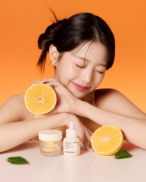 A clean, high-contrast product photography shot featuring a skincare serum and cream alongside halved citrus fruits to signify natural brightening ingredients.