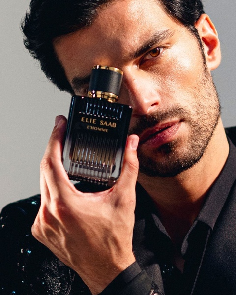 A high-fashion, intimate close-up of a model holding a luxury men's fragrance bottle to create an aura of exclusivity.