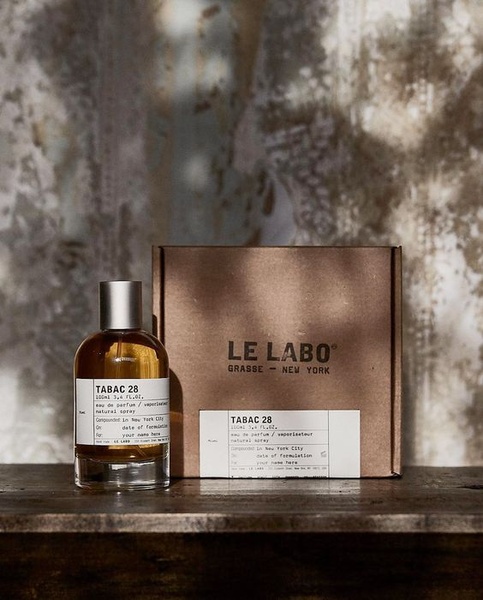 A high-end, minimalist presentation of a perfume bottle placed next to its textured, branded box, utilizing warm natural light.