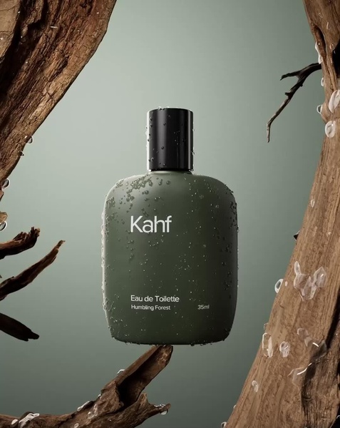 A high-quality studio shot of a perfume bottle framed by raw wood branches and water droplets against a muted green background.