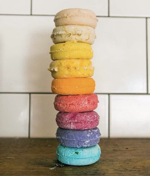 A vertical, balanced stack of eight colorful shampoo bars against a clean, white tiled background.