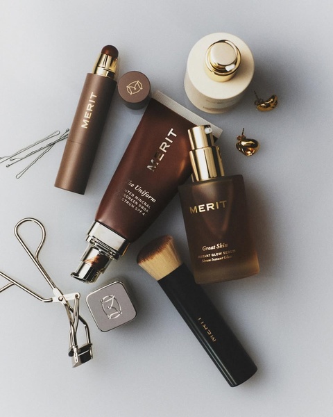 A high-end, top-down flat lay featuring premium cosmetic skincare bottles, brushes, and accessories on a neutral, professional studio background.