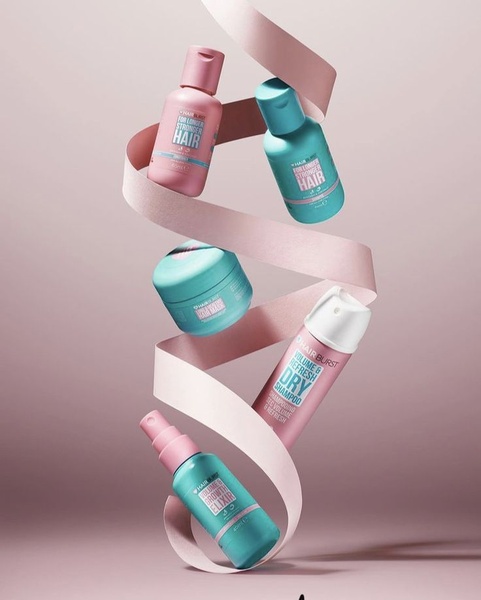 A high-end product photography style ad featuring five distinct hair care bottles and jars suspended in a minimalist studio environment with a flowing ribbon.