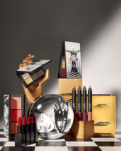 A luxury-themed product display featuring multiple cosmetic items like lipsticks, palettes, and pencils arranged on a checkered surface with a golden hand, emphasizing high-end aesthetics.