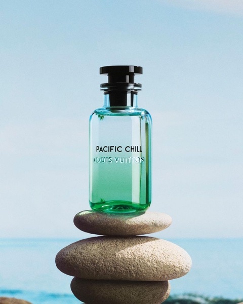 A high-end visual advertisement featuring a perfume bottle balanced on stacked river stones against a soft blue sky background to convey a sense of calm.