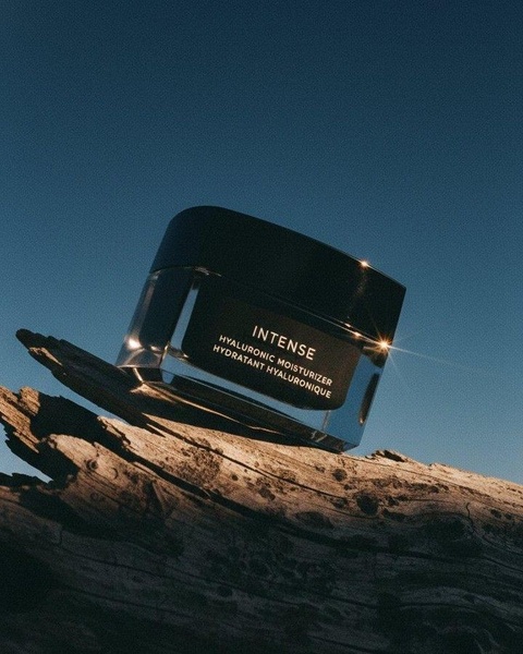 A high-end skincare moisturizer jar is positioned on weathered driftwood against a deep blue sky to evoke a premium, organic feeling.
