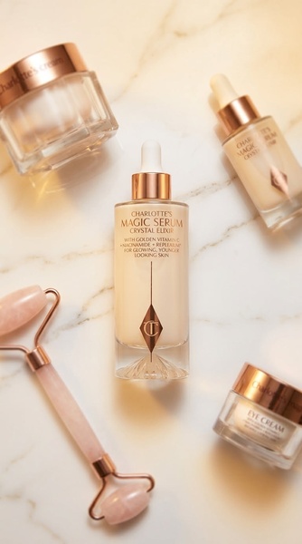 A high-end flat lay featuring a serum bottle centered between a face cream, eye cream, and quartz roller on a marble background.