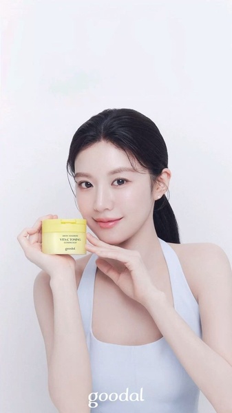 A clean, high-key studio portrait featuring a model holding a jar of Vitamin C toning cream, emphasizing a natural and healthy glow.