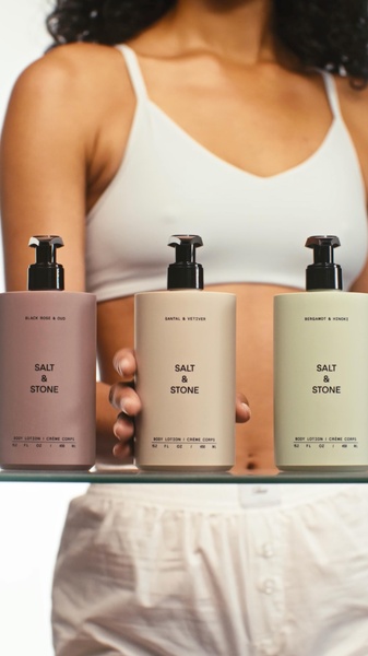 A close-up, high-quality shot of a person holding three body lotion bottles in distinct neutral shades.