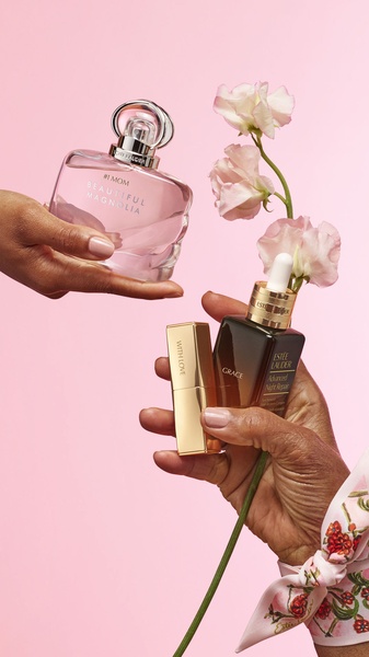 A high-end, aesthetic composition featuring perfume and skincare bottles held by hands against a soft pink background, emphasizing gifting and luxury.