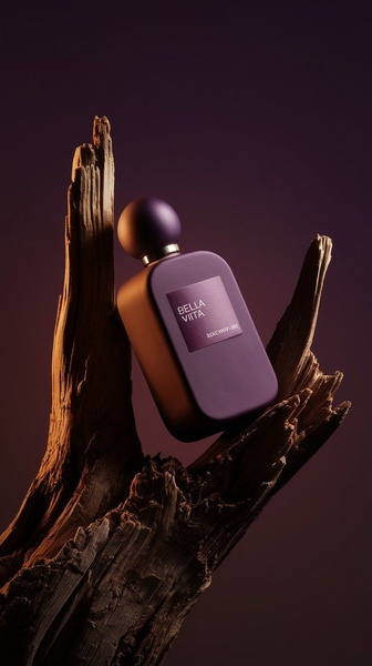A high-end, minimalist product shot featuring a dark purple perfume bottle resting on a piece of weathered driftwood against a moody, deep violet background.