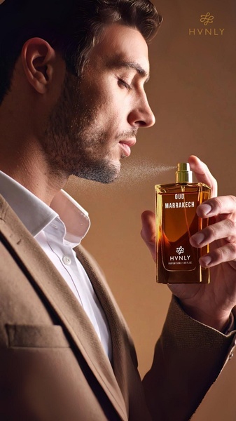 A close-up portrait of a man applying a luxury perfume, highlighting the bottle and the act of application in a warm, professional setting.