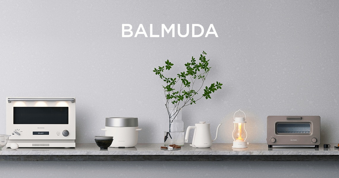 A high-end, static product display showcasing a collection of premium kitchen appliances on a marble countertop against a soft grey textured wall.