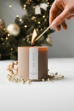 A close-up shot of a hand lighting an Apple Pie scented candle, surrounded by holiday decorations, capturing a cozy, seasonal atmosphere.