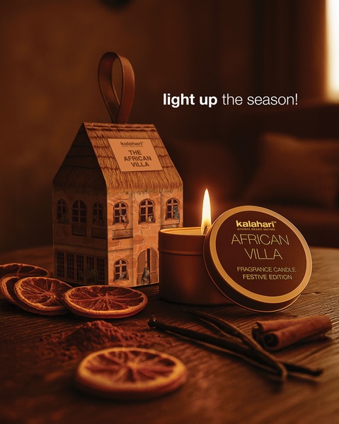 A high-quality product shot of a festive edition fragrance candle, complete with thematic packaging, dried orange slices, and spice elements on a dark wooden surface.