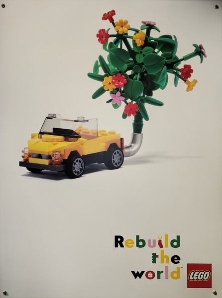 A yellow toy car is shown from a profile view with a vibrant plastic flower growing from the rear exhaust, symbolizing creativity and rebirth.