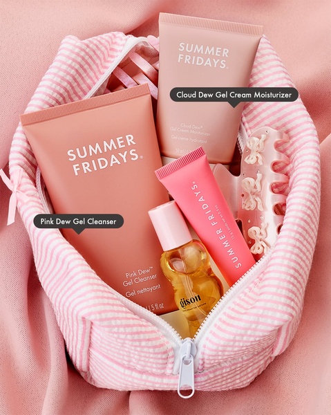 A top-down, organized flat lay showcasing a collection of pink-themed skincare products inside a matching striped travel bag.
