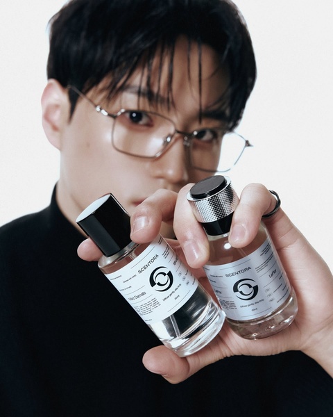 A close-up, high-fashion shot featuring a model holding two elegant perfume bottles against a clean, white, minimalist background.