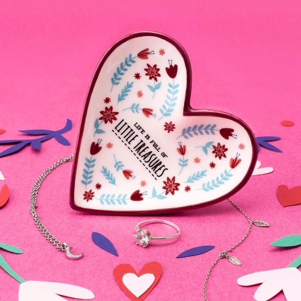 A heart-shaped ceramic tray with floral motifs serves as the central focal point, surrounded by delicate jewelry on a vibrant pink background.