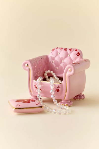 A high-end, studio-lit photo of a miniature pink porcelain armchair used as a charming jewelry box, adorned with a delicate pearl necklace.