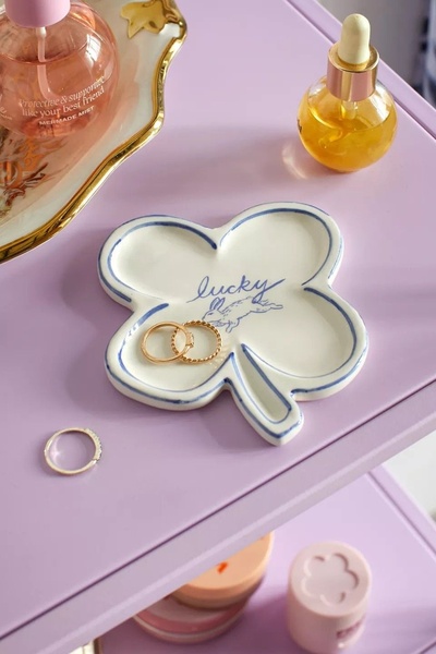 A high-quality lifestyle shot featuring a clover-shaped ceramic trinket tray on a pastel surface, designed to evoke a clean and organized aesthetic.